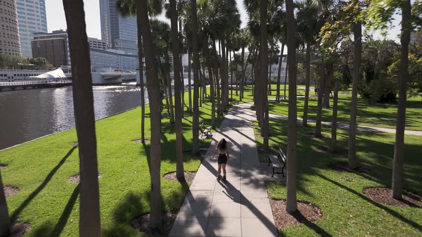 A woman roller skates on a city park sidewalk on a sunny summer day