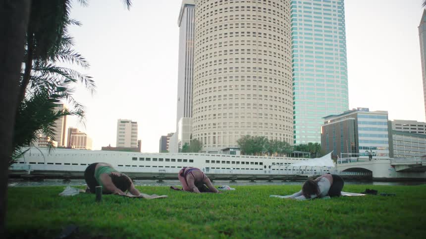 Women stretching on yoga mats on the lawn near a river in the city