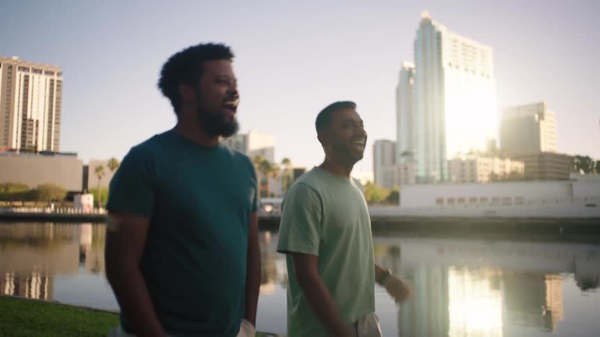 Two men walking on grass in an outdoor setting by a lake
