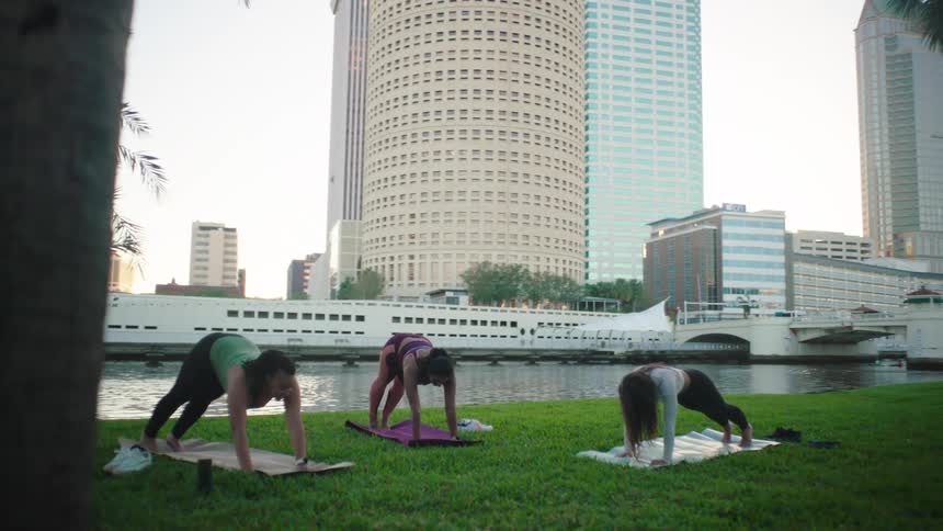 Three women outdoors practicing yoga in a park on the grass
