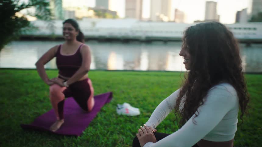 Three women are stretching on exercise mats next to a river