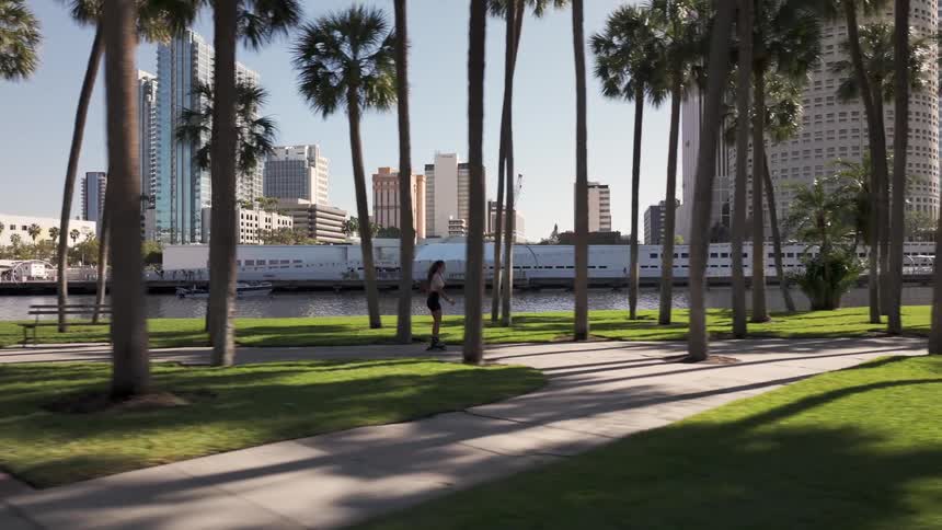 Woman rollerblading through a park lined with palm trees and a lake