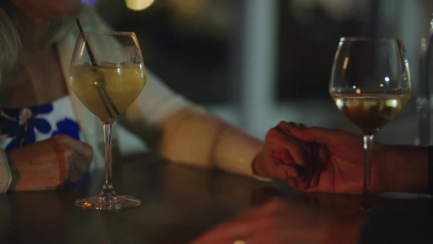 A man and woman hold hands and drink wine outside