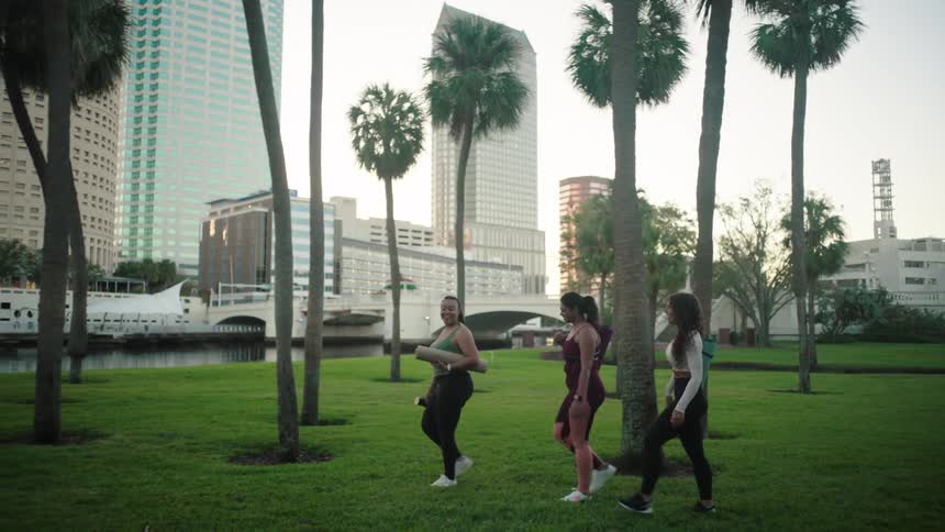 Three women in yoga clothes walking in a park with trees and grass