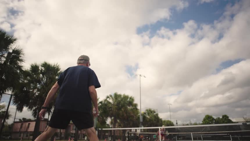 Elderly man holds pickleball racket during a game on an outdoor court