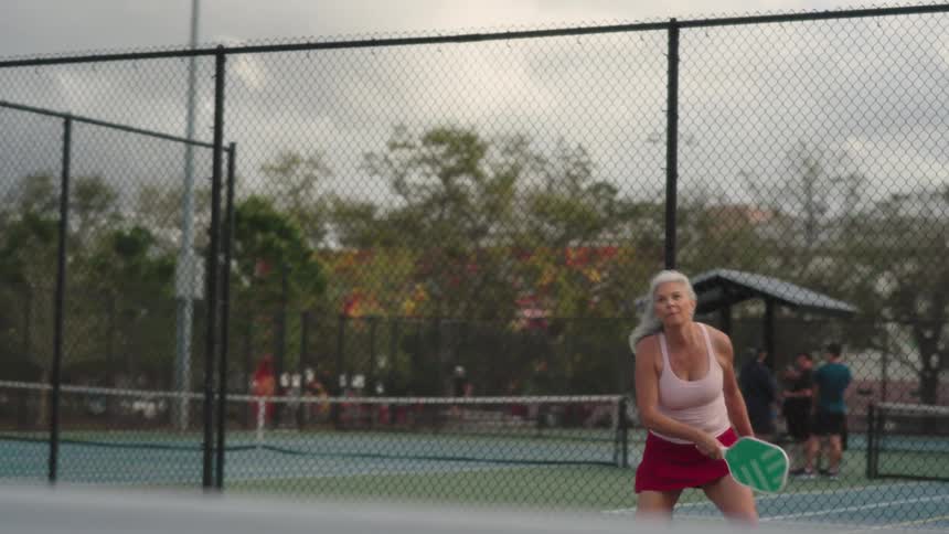 Elderly woman playing tennis on an outdoor court