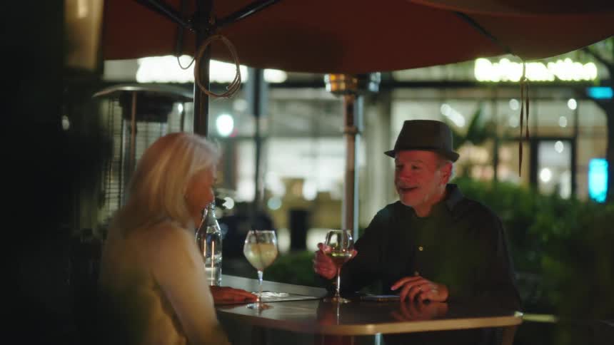 A man is talking with a woman while they drink wine