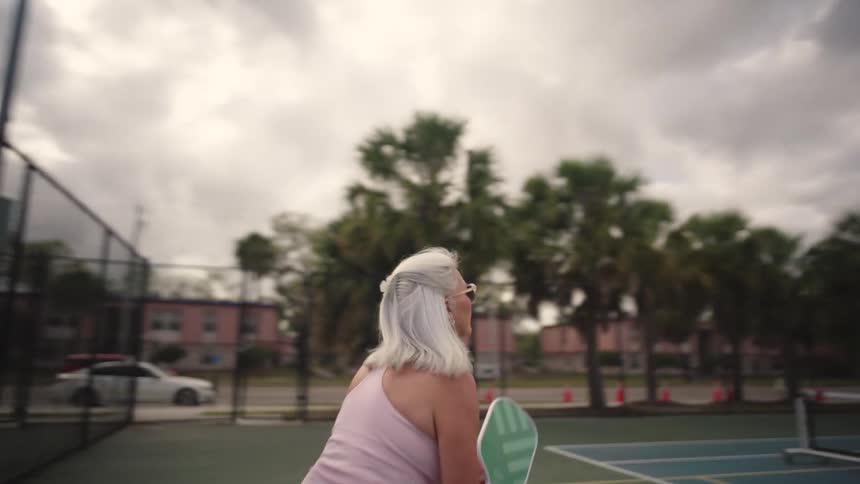 A woman is running and playing pickleball