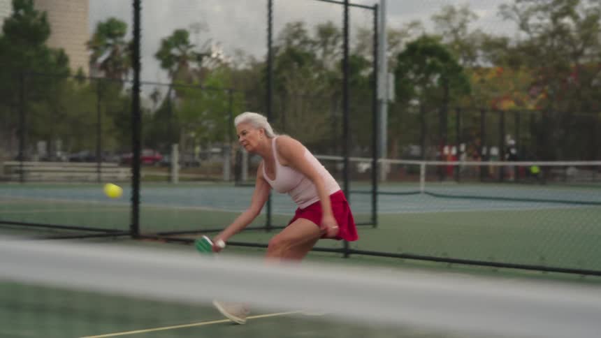 Elderly woman plays pickleball on outdoor court
