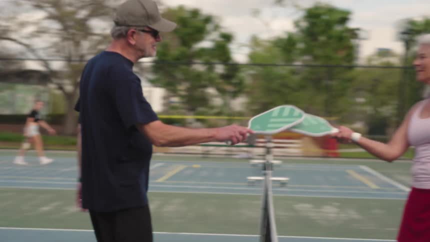 Man and a woman hitting tennis rackets while standing on an outdoor court