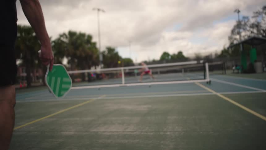 Man and woman play pickleball on a court in the park on a cloudy summer day