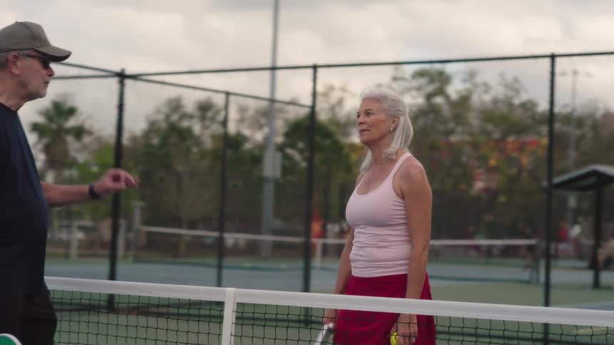 Man and a woman greet each other with a racket on an outdoor court