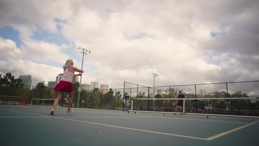 Two older people play pickleball on a cloudy summer day