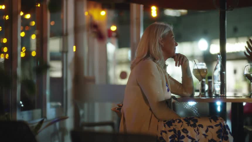 Elderly woman sitting at an outside restaurant table with a drink chatting