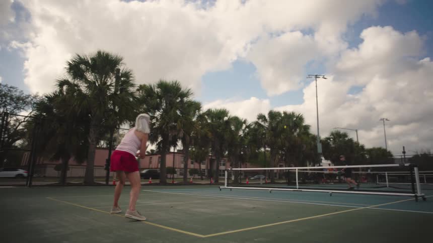 Man and woman on an outdoor tennis court playing a game of pickleball