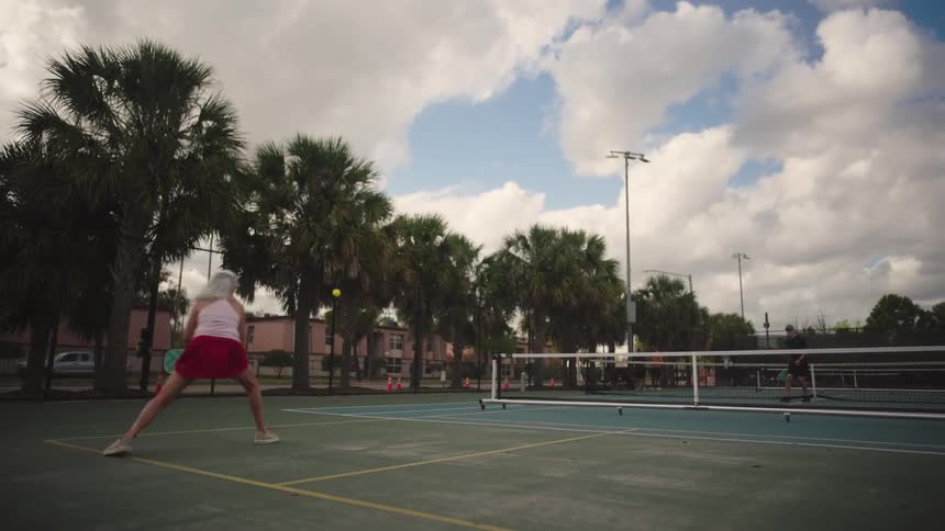Elderly woman and another person playing pickleball in an outdoor area