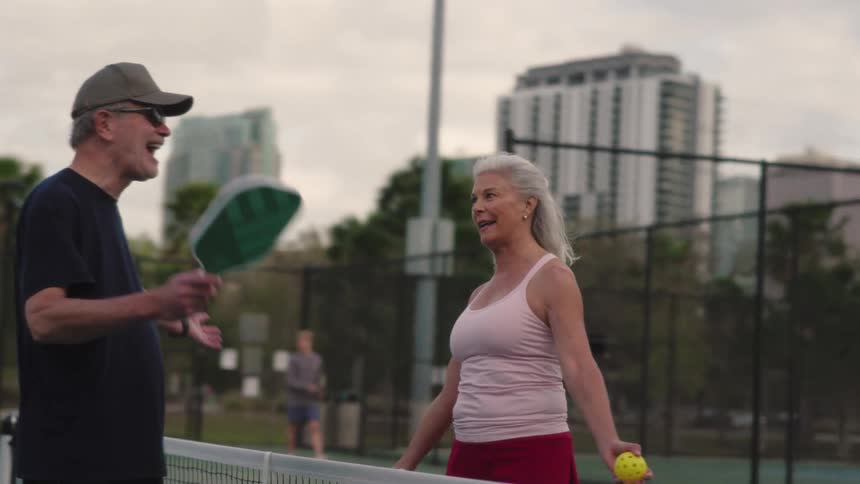 Elderly couple playing pickleball outdoors holding rackets