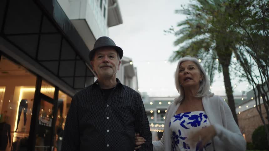 An elderly couple talks as they walk through a business area