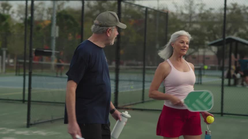 Couple walking on an outdoor court with pickleball rackets