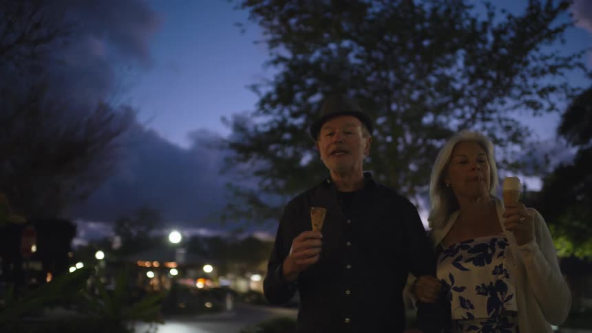 Elderly couple walking and eating ice cream at dusk