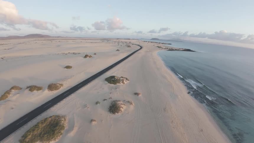 Aerial of a remote highway that runs along an ocean coast under partly sunny skies