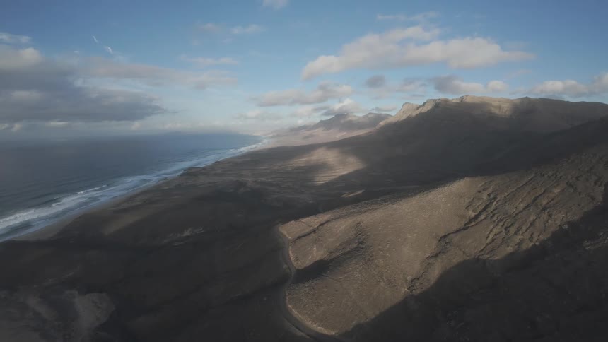 The waves crash on the beach by the mountains