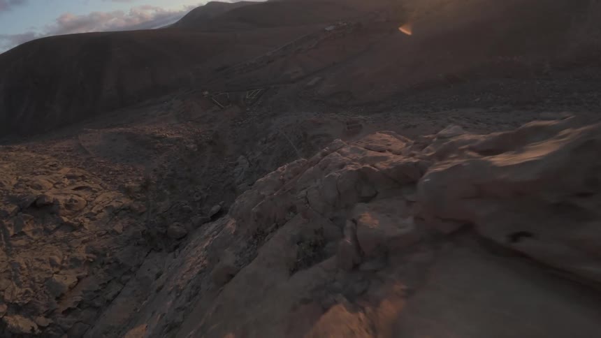 Aerial view of a rock covered mountain range and the sun shining on it