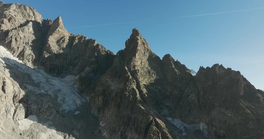 A rugged rocky mountain range under a clear blue sky with patches of snow visible on the slopes