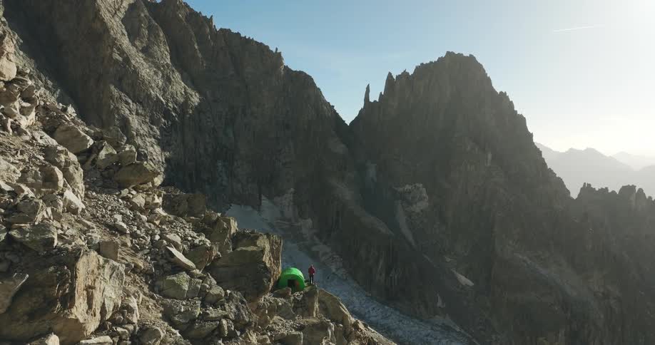 Person with a tent on a mountain cliff at sunrise