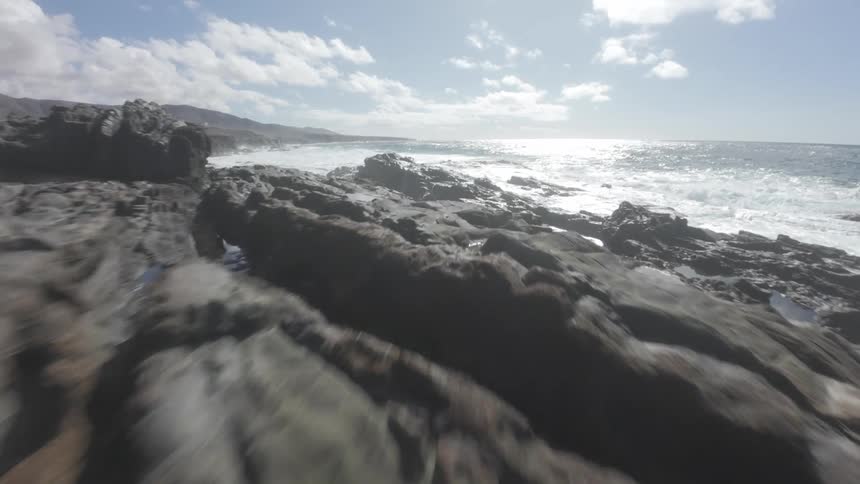 A rugged rocky coastline with cliffs overlooking a turquoise pool of water and the open ocean under a partly cloudy sky