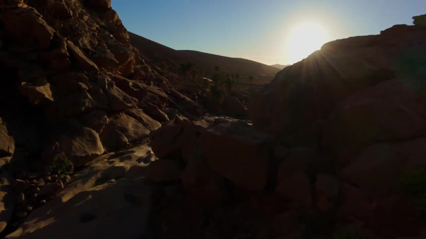 A dramatic sunlit canyon landscape with rugged rock formations and a distant mountain range