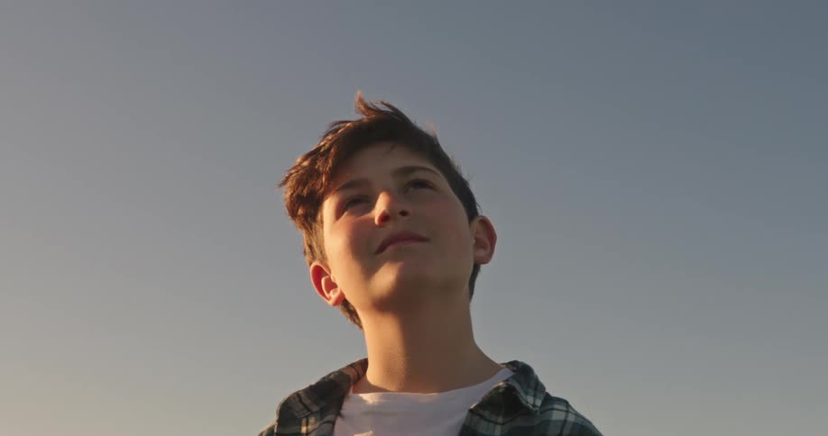 A teenage boy smiles while standing outdoors and looking up at the sky