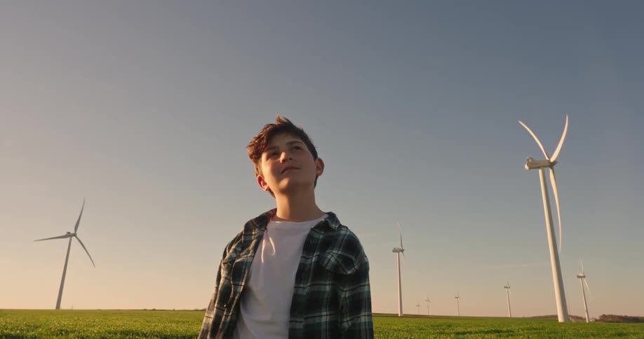 Boy smiles while standing between the wind turbines at a wind farm and looking up
