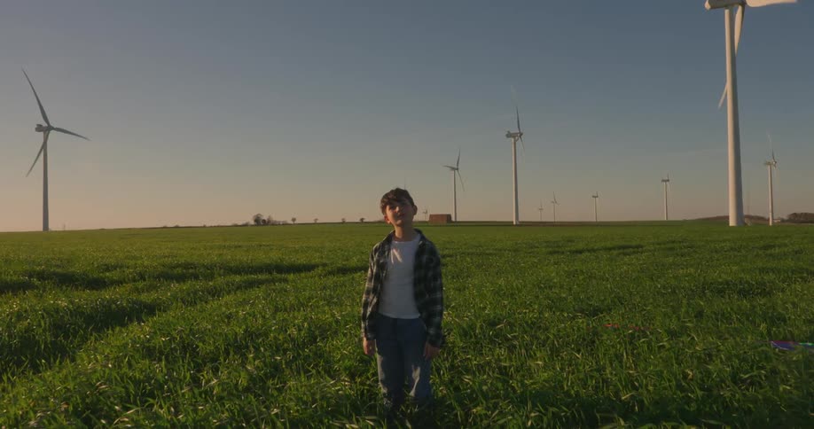 A footage of a boy standing on a wind turbine field