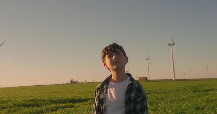 Boy stands at a wind farm looking up at the turbines on a sunny day
