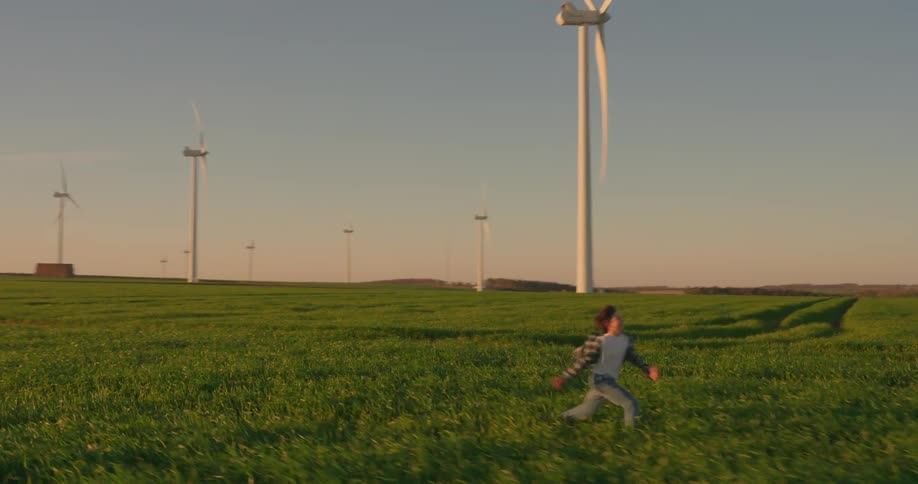 Boy runs through the field between the wind turbines at a wind farm on a sunny day