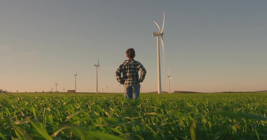 A footage of a boy standing and looking at a wind turbine
