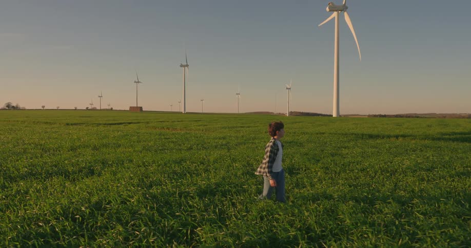 Boy walking through an agricultural field with wind power platforms in the background