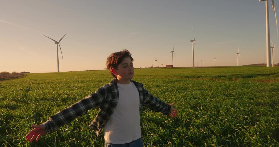 Boy with eyes closed and arms open while standing in a farm field with wind power platforms