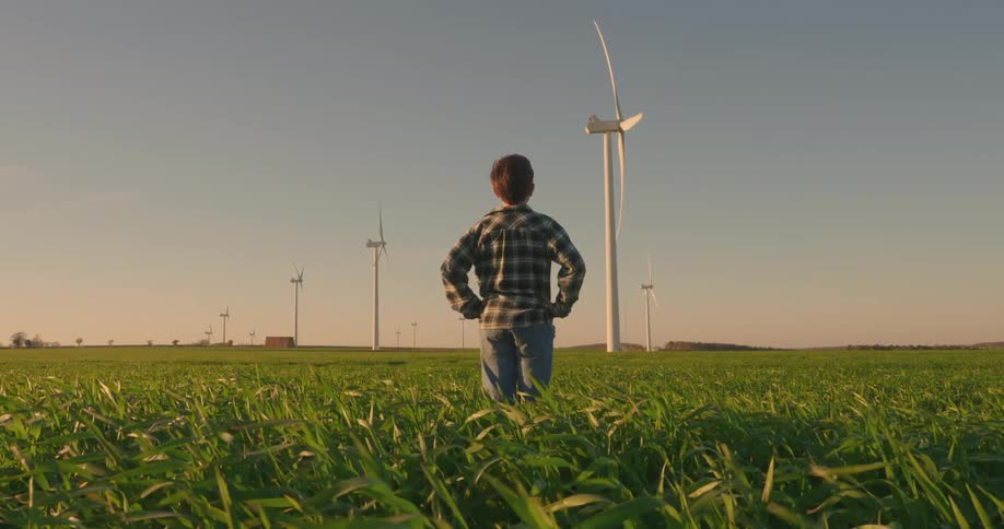 Boy with hands on hips in an agricultural field watching wind power engines