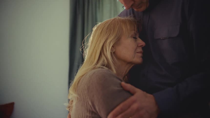 Sad man comforts his equally sad wife by hugging her and rubbing her arms