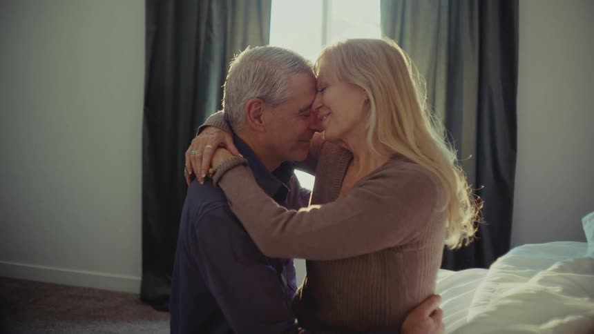 Man and woman lovingly hug each other while sitting on a bed