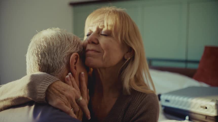 A man and woman hug while sitting on the bed