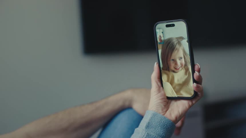 A couple of parents sit comfortably at home holding a phone while on a video call with their young daughter