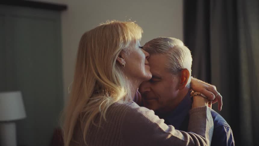 A senior couple are hugging in a room