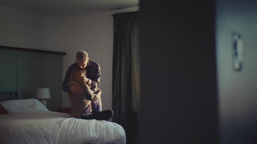 A man hugs and kisses a woman sitting on the bed