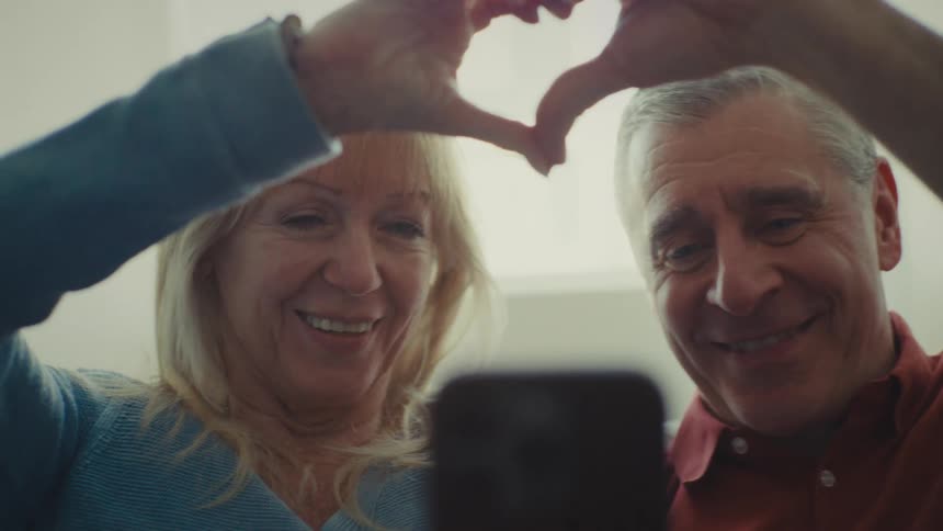 A man and woman use their hands to make a heart gesture on a video call