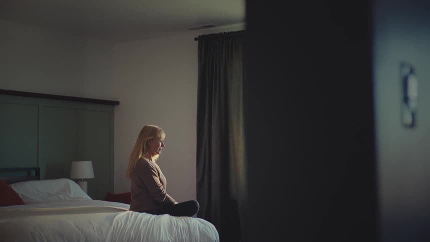 A woman is sitting on the bed looking out the window