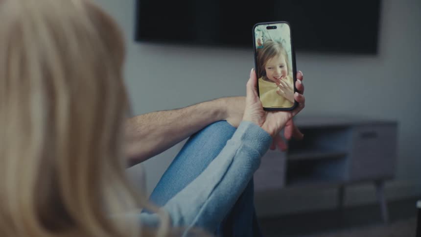A couple of parents sit comfortably at home holding a phone while on a video call with their young daughter