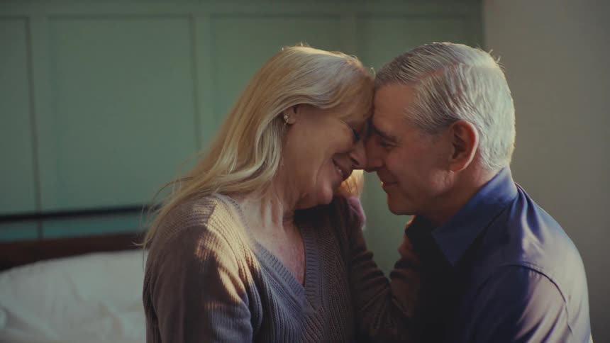 A footage of an older man and a woman sharing an affectionate moment together in a room